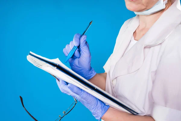 Medico donna adulta facendo note nel suo file su uno sfondo blu — Foto Stock