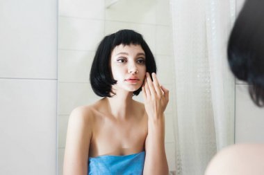 Siyah saçlı genç kız kendini aynada inceliyor