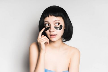 kısa siyah saçlı bir kız maske gözleri altında gri bir arka plan üzerine koyar.