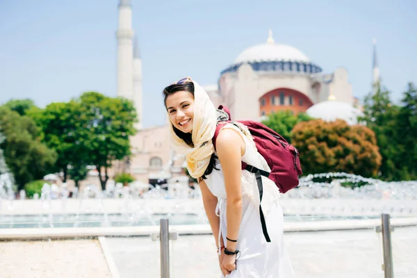 A young woman in a scarf with a backpack on the background of Aya Sofia and a fountain laughing. Summer vacation, traveler — Stock Photo, Image