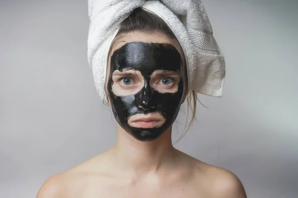 Cuidado da pele da mulher, cosméticos máscara preta no rosto. Toalha na cabeça — Fotografia de Stock