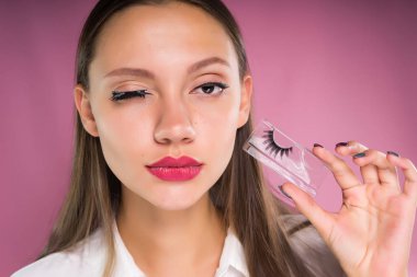 Genç kız pembe bir arka plan üzerinde sahte kirpik koyar