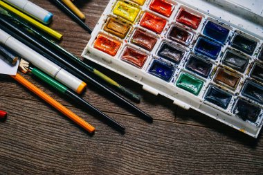 ahşap yüzeyde sanatsal aksesuarlar, suluboya, kurşun kalem ve tükenmez kalem vardır