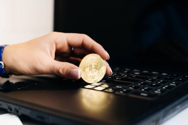 Kız yatırımcı elinde altın bitcoin bir dizüstü bilgisayar arka plan, kripto para birimi hakkında düşünüyor üzerinde tutar.