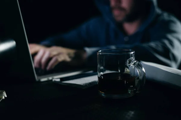 Homme criminel mystérieux dans un capot pirater quelque chose sur un ordinateur portable dans l'obscurité — Photo