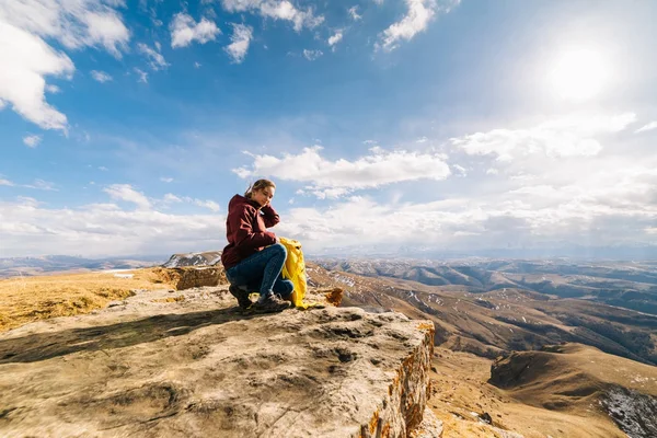 Active young girl loves sports tourism, sits on the edge of the mountain in the rays of the sun — Stock Photo, Image