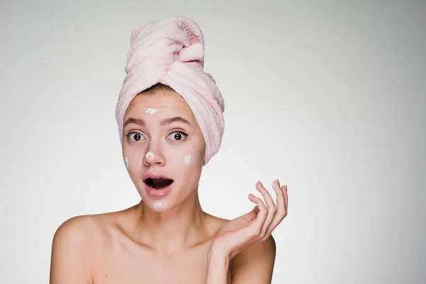 Überrascht junge Mädchen mit einem rosa Handtuch auf dem Kopf trug eine nützliche weiße Creme auf ihr Gesicht — Stockfoto