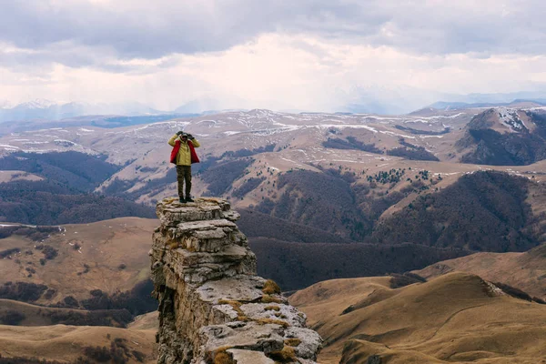 Male traveler in a red jacket stands on the edge of a cliff, enjoying nature and mountains — Stock Photo, Image