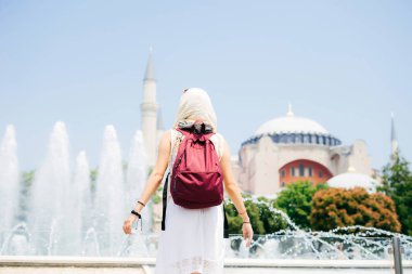 Bir eşarp ile cami ve Çeşme bir arka plan üzerine bir sırt çantası içinde tanınmayan bir kadın. Yaz tatili, gezgin