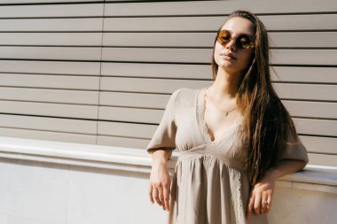 gözlük takan yaz elbiseli genç kız sokakta bir duvara eğilir