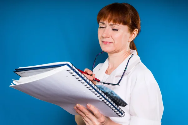 Женщина на синем фоне в медицинском халате осматривает документы — стоковое фото