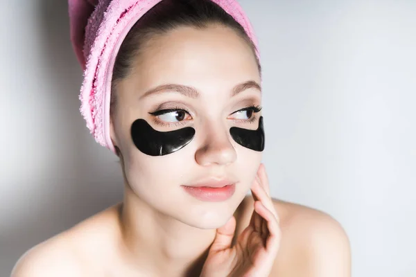 Молодая девушка с полотенцем на голове улыбается, нанося черную маску на лицо — стоковое фото