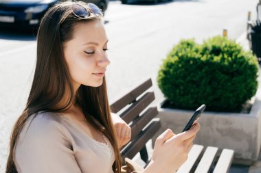 genç bir kız bir bankta oturur ve telefonda metni yazdırır