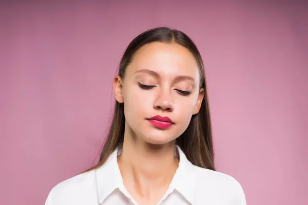 Virada menina de pé em um fundo rosa fechando os olhos — Fotografia de Stock