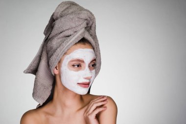 Kafasındaki bir havlu ile çekici bir genç kız bir besleyici beyaz maske yüzüne karşı uygulanan.
