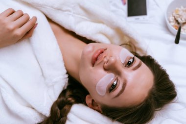 güzel genç kız sabahın erken saatlerinde, yulaf lapası, beyaz lekeler gözleri altında bir tabak yanındaki yatakta yatıyor