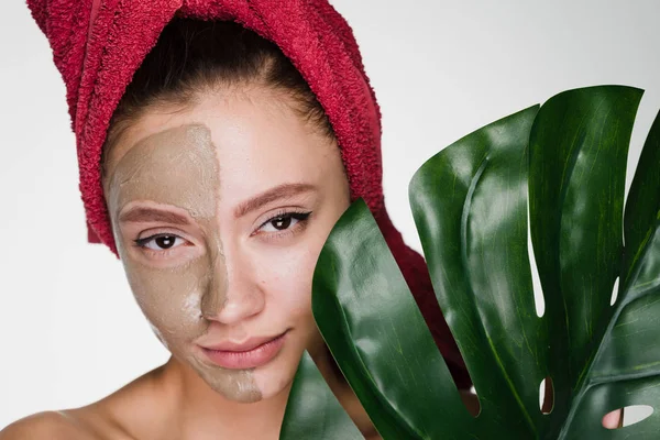 Μια ελκυστική νεαρή κοπέλα θέλει καθαρή δέρματος, θέσει στο μισό πρόσωπο μία μάσκα αργίλου χρήσιμο — Φωτογραφία Αρχείου