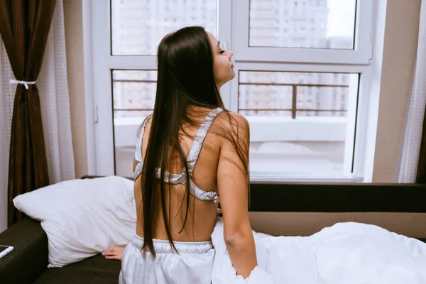 Chica de pelo largo se despertó temprano, se sienta en la cama y no quiere levantarse — Foto de Stock