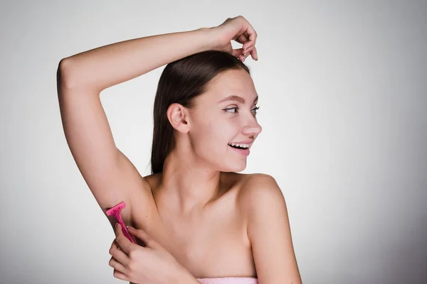 Beautiful smiling girl shaves her armpits with a pink razor — Stock Photo, Image