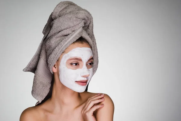 Привлекательная молодая девушка с полотенцем на голове надела питательную белую маску на лицо — стоковое фото