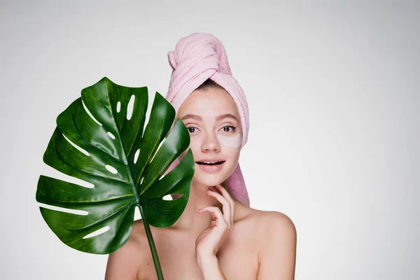 Linda chica hermosa con una toalla en la cabeza sosteniendo una hoja verde, spa de día, bajo los ojos parches — Foto de Stock