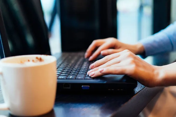 Ragazza freelance lavorando su un computer portatile, in un caffè, sul tavolo è una tazza di caffè delizioso — Foto Stock