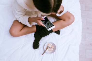 bir kız sabah bir yatakta oturur ve onu elinde bir telefon vardır