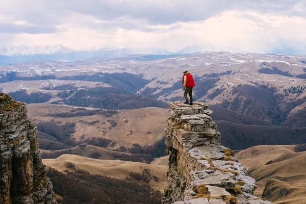 A young man in a red jacket stands at the edge of a cliff — Stock Photo, Image