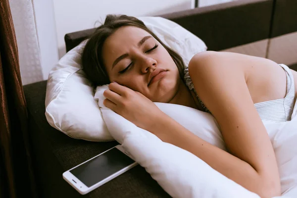 A jovem está dormindo ao lado do telefone — Fotografia de Stock