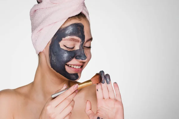 girl with a towel on her head applies a black mask to clean the face