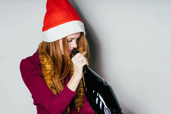 Das Mädchen mit der Neujahrsmütze hält eine Flasche Wein in der Hand — Stockfoto