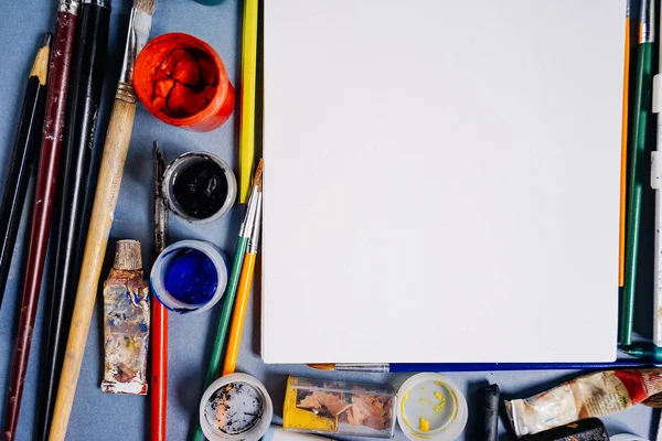 Hoja blanca de papel sobre un fondo de pinturas multicolores con pinceles — Foto de Stock