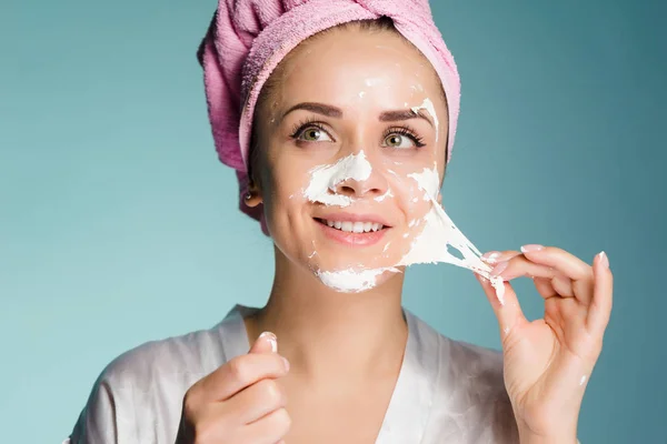 Chica después de la ducha con una toalla en la cabeza quita la máscara de limpieza de la cara — Foto de Stock