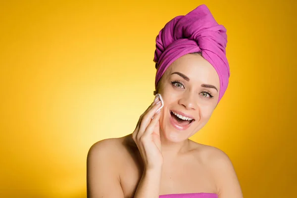 Ευτυχισμένος κορίτσι με μια πετσέτα στο κεφάλι της αφαιρεί το μακιγιάζ με ένα δίσκο βαμβακιού — Φωτογραφία Αρχείου