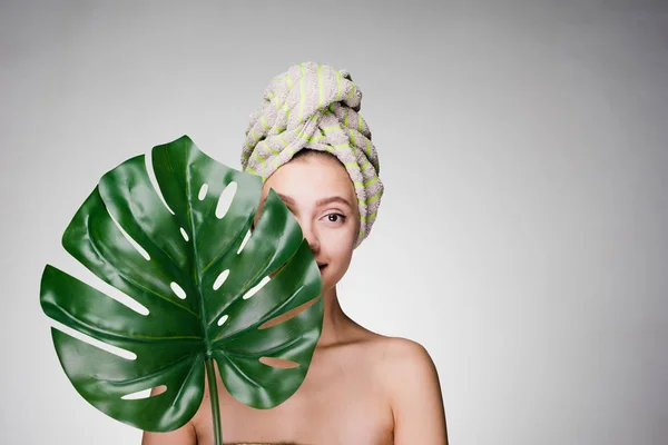 Chica con una toalla en la cabeza después de limpiar su piel de la cara sostiene una hoja grande — Foto de Stock