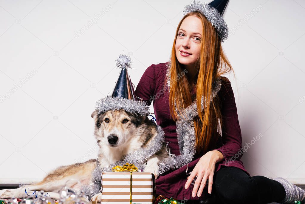 the girl in a festive cap sits next to the dog