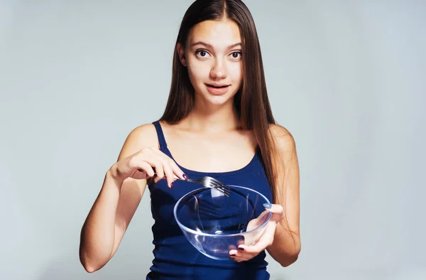 Beautiful young girl in a blue top sits on a diet, holds a glass plate in hands — Stock Photo, Image