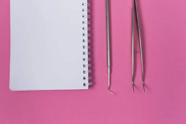 Auf einer rosa Oberfläche befinden sich ein weißes Notizbuch und zahnärztliche Instrumente — Stockfoto