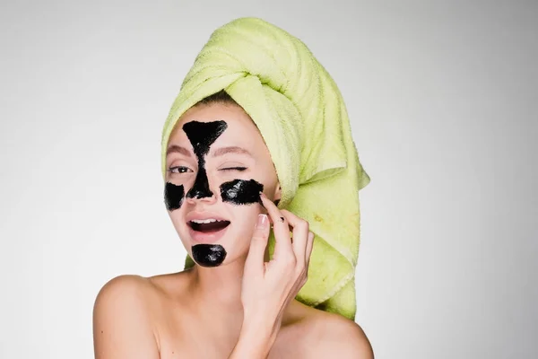Όμορφη κοπέλα χαμογελαστή με μια πράσινη πετσέτα αφαιρεί ένα μαύρο καθαρισμού μάσκα από το πρόσωπό της — Φωτογραφία Αρχείου