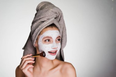 Kafasındaki bir havlu ile çekici genç kız yüzünü bir fırça ile beyaz bir maske koyar