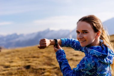 güzel genç mavi bir ceket ve gezgin bir kol saati, Kafkas Dağları'nın arka planı gülümsüyor zaman gösterir