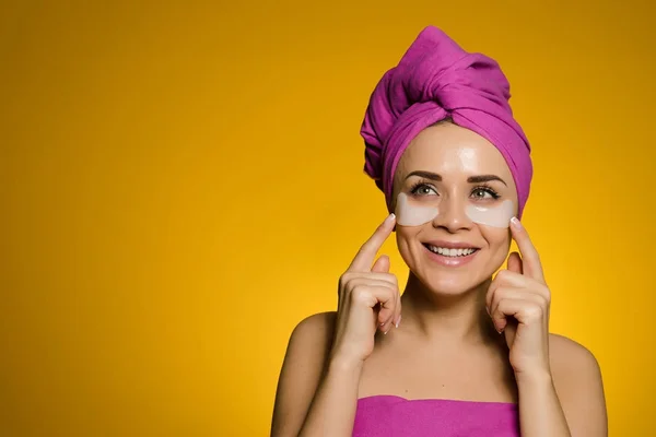 Sorridente bella ragazza con i denti bianchi, sulla testa un asciugamano rosa, sotto gli occhi macchie bianche — Foto Stock