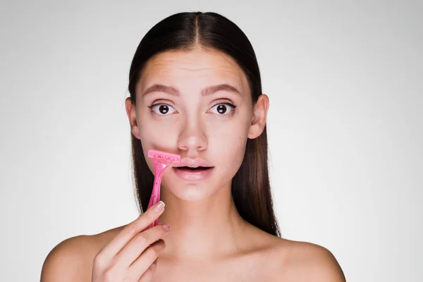 Jovem menina atraente barba um bigode com uma navalha rosa — Fotografia de Stock