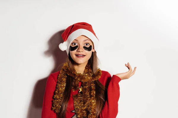 Feliz hermosa chica en una gorra roja como Santa Claus esperando el nuevo año 2018, bajo los ojos de parches negros —  Fotos de Stock