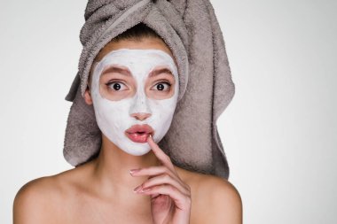 Kafasındaki bir havlu ile komik sürpriz bir kız beyaz bir besleyici maske yüzüne karşı uygulanan.