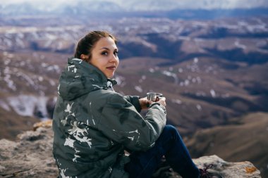 genç bir kız dağ kenarında oturur, sıcak çay içiyor ve doğa sever