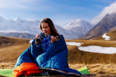 bir uyku tulumu Kafkas Dağları'nın arka plan üzerinde oturan gülümseyen genç kız Gezgin
