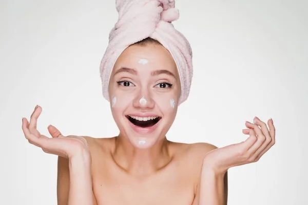 Förvånad glad tjej med en handduk på huvudet sätter i ansiktet som vårdande kräm — Stockfoto