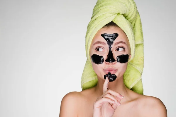 En rolig ung flicka med en grön handduk på huvudet tillämpas en svart cleansing mask mot acne i ansiktet — Stockfoto