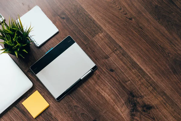 En la superficie de madera es un ordenador portátil para el trabajo, una tableta gráfica y una planta verde en una olla — Foto de Stock